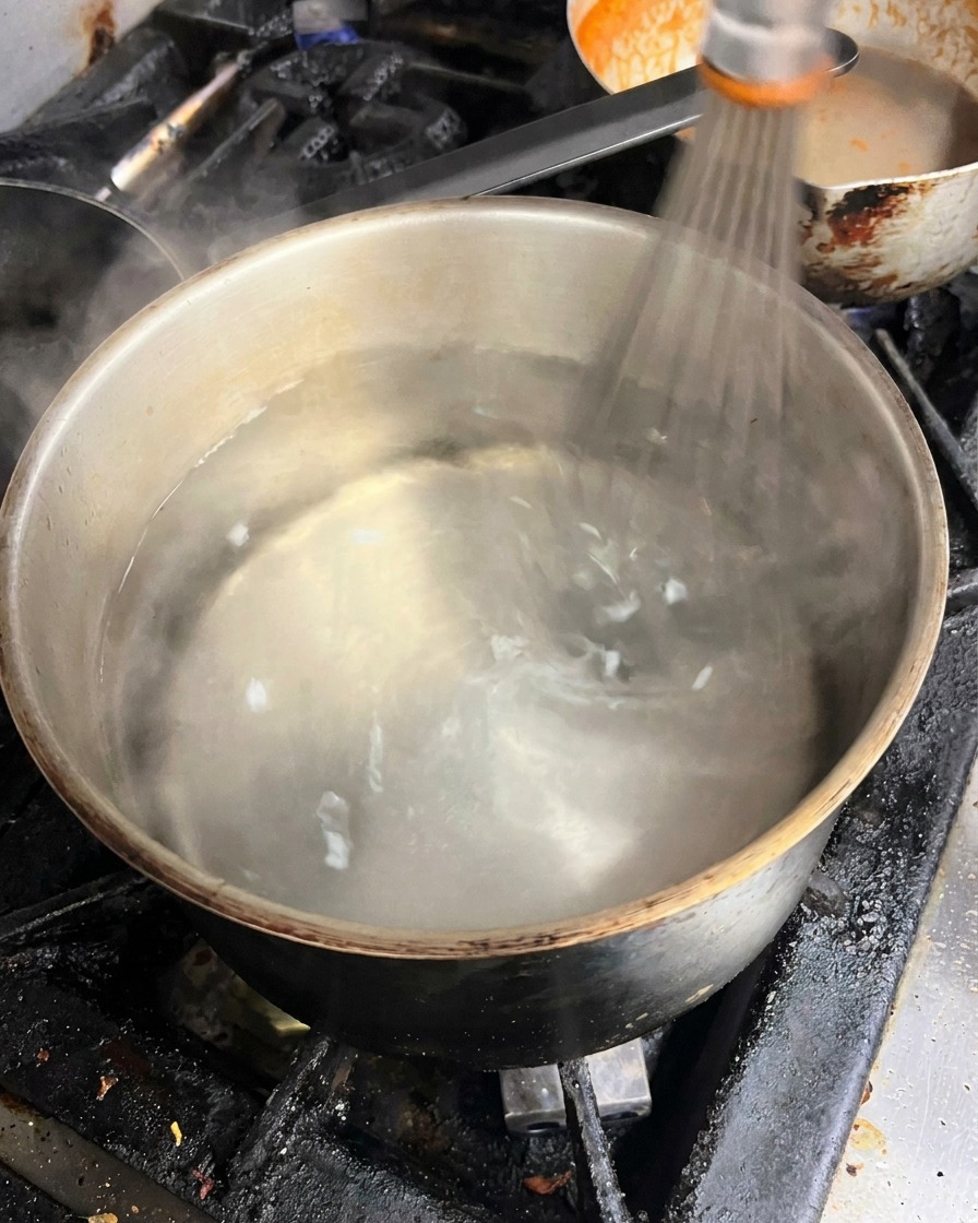 Wasser in einem Topf wird mit einem Schneebesen zu einem Strudel gerührt.