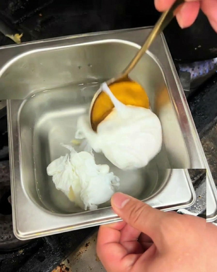Ein fertig pochiertes Ei wird mit einem Löffel aus dem Wasser gehoben.