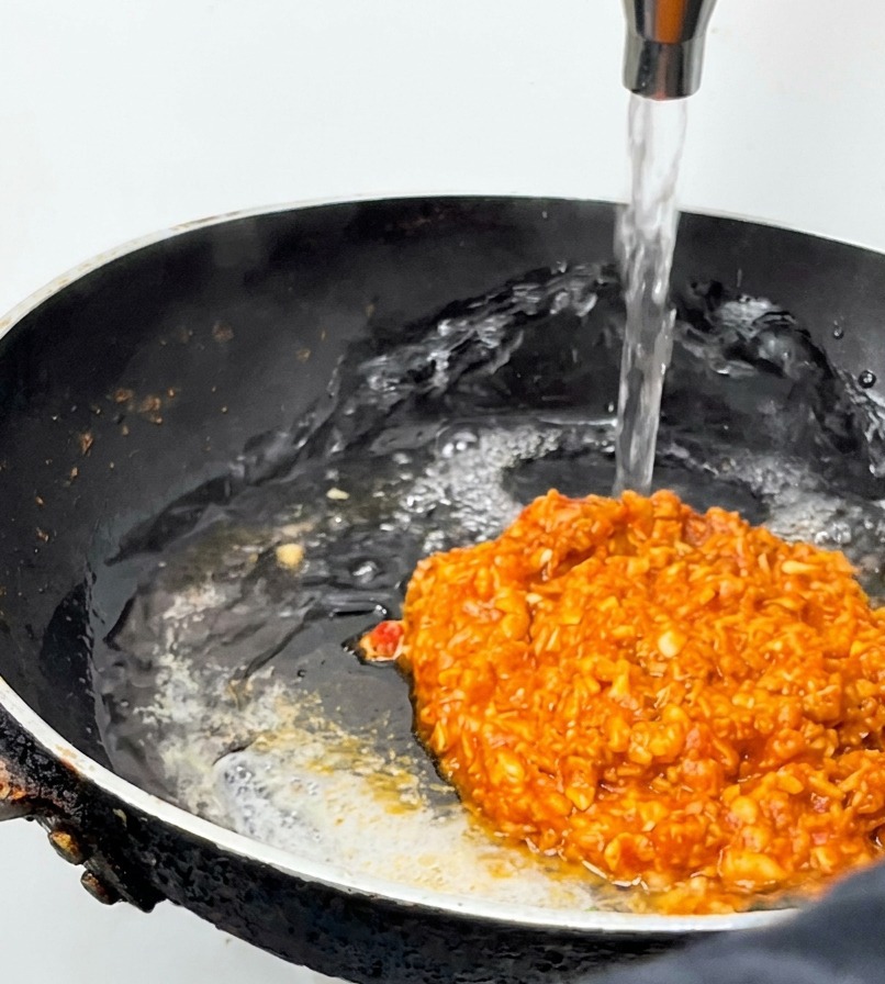 Wasser wird in die Pfanne zur köchelnden Fleischsauce gegossen.