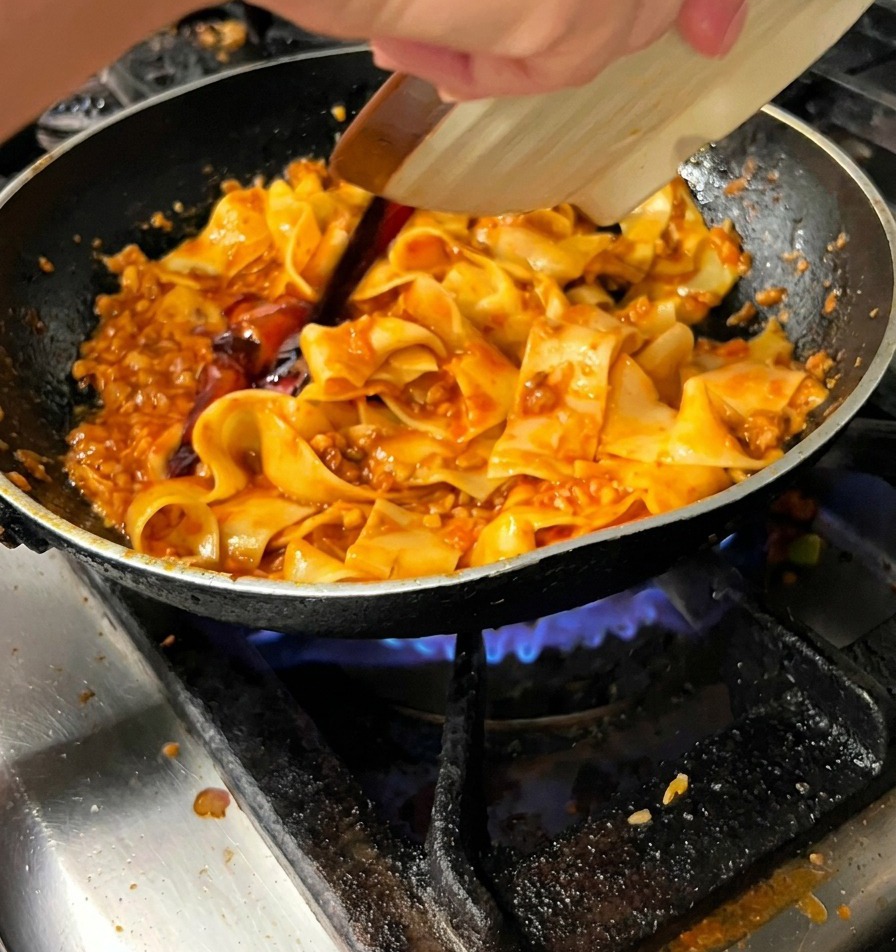 Dunkle Sauce wird über die Pappardelle in der Pfanne gegossen.