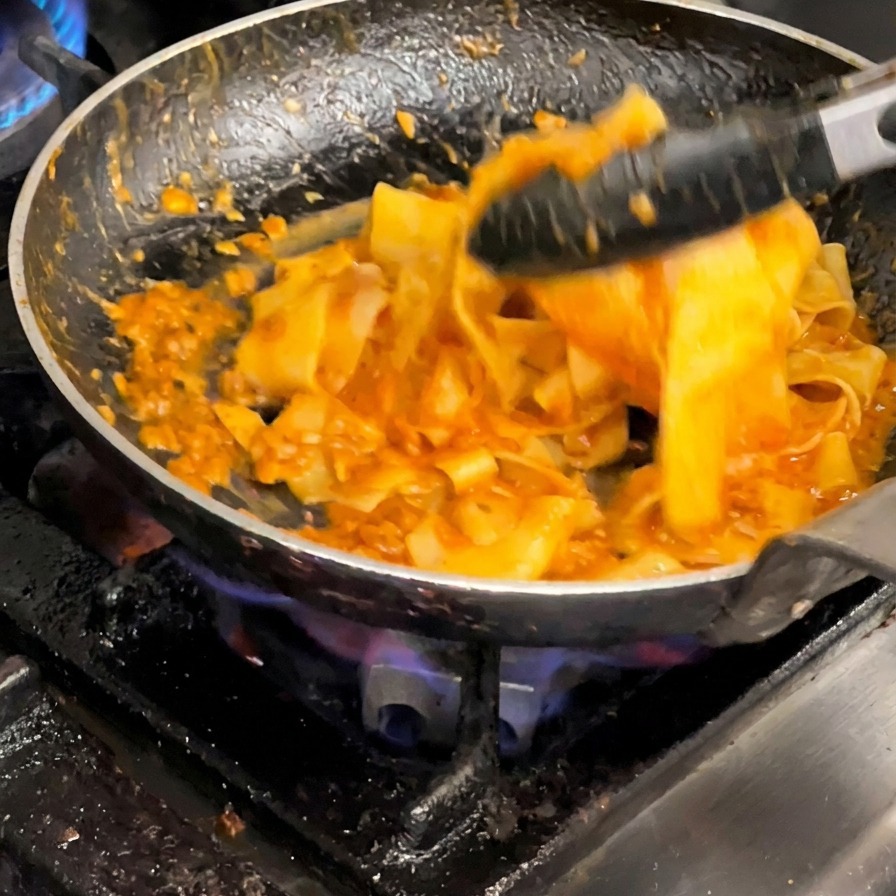 Mit einer Zange werden die Nudeln kräftig mit der Sauce vermengt.