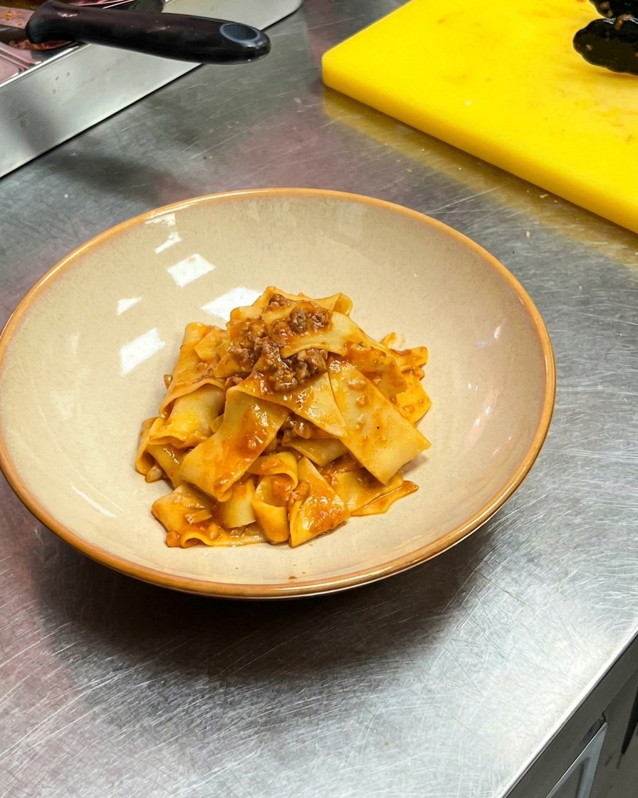 Eine Zange legt die Fleischsauce-Pappardelle in eine Servierschale.