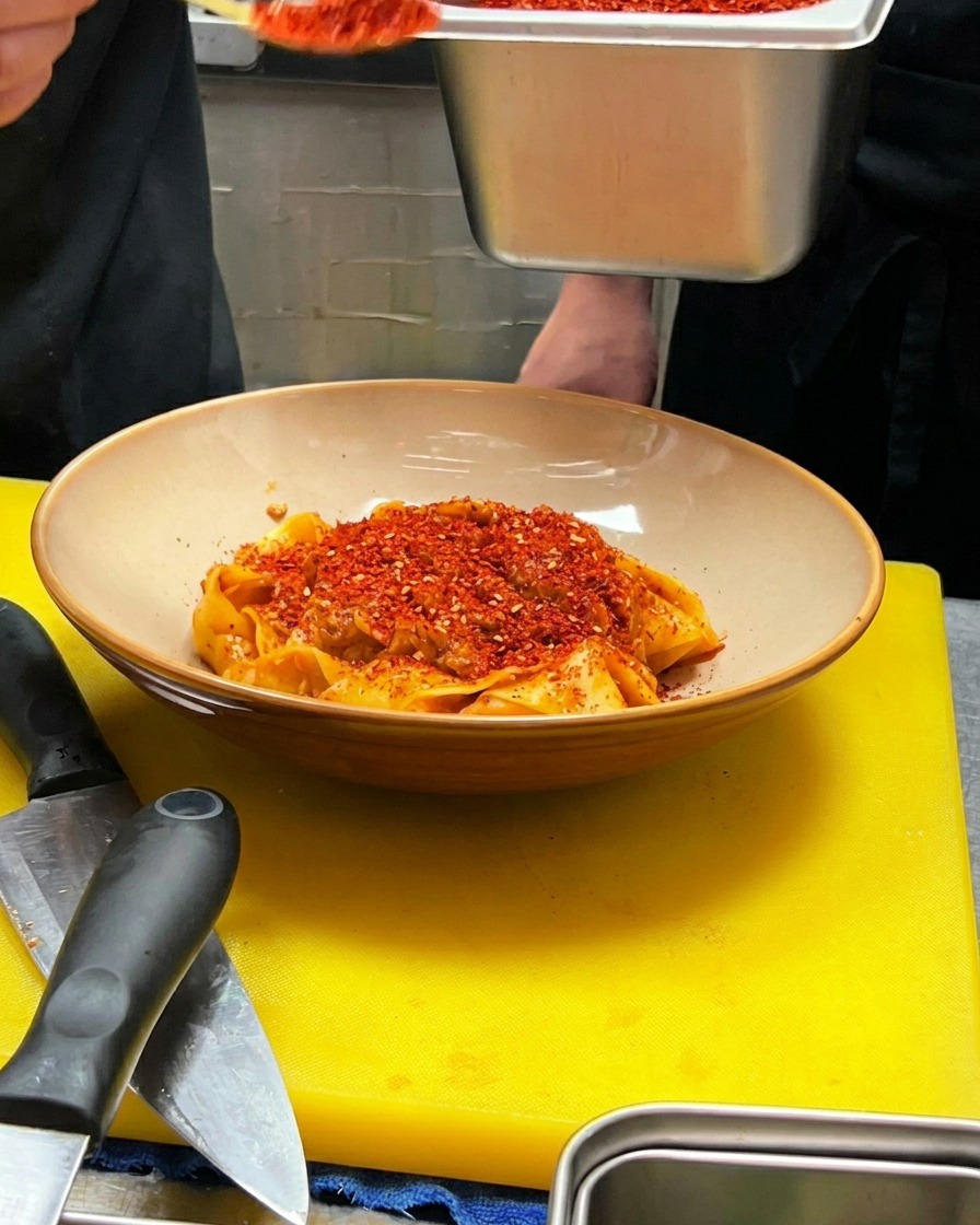 Ein Löffel rotes Chilipulver wird in die Mitte der angerichteten Pasta gegeben.