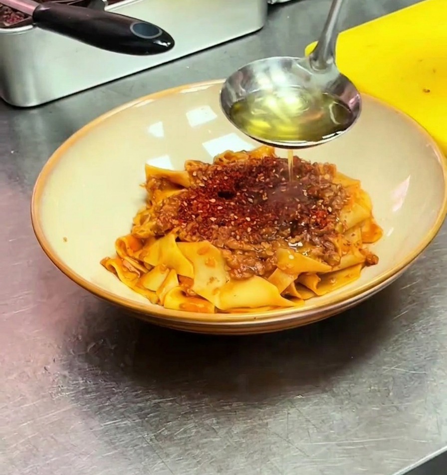 Heißes Öl wird aus einer Kelle über das Chilipulver auf der Pasta gegossen.