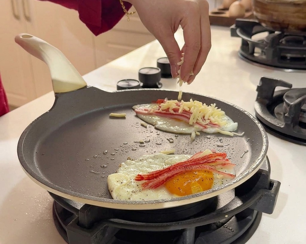Eine Hand streut geriebenen weißen Käse über die bratenden Eier und das Surimi.