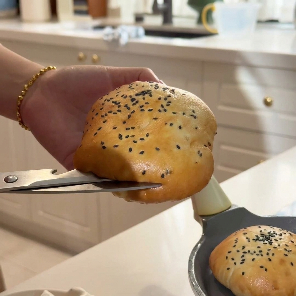 Eine Hand schneidet ein warmes Sesabbrötchen vorsichtig mit einer silbernen Küchenschere auf.