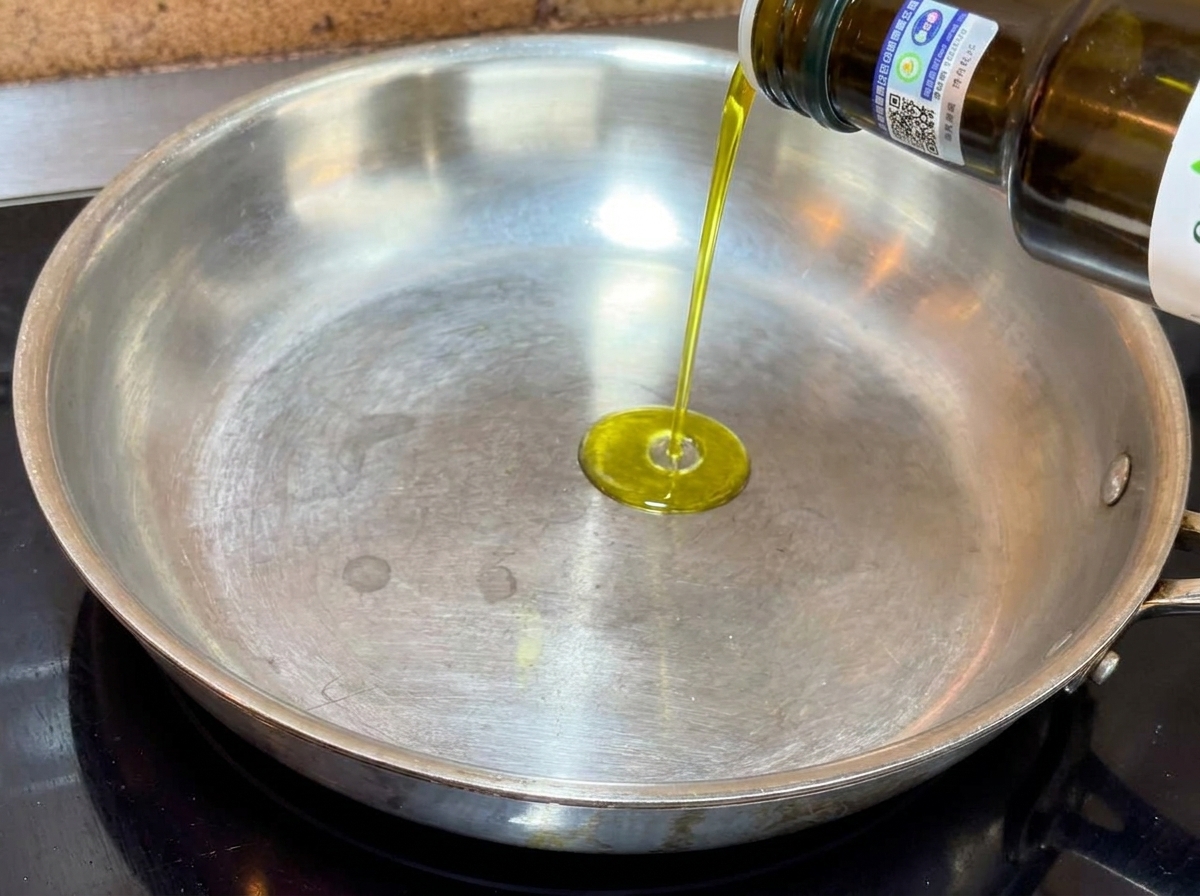 Natives Olivenöl extra wird aus einer Flasche in eine flache Metallpfanne gegossen.