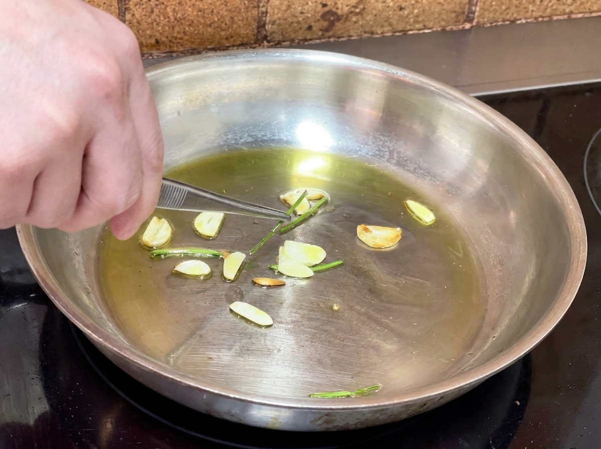 Eine Metallpinzette nimmt frittierte Petersilienstiele aus einer Pfanne mit Knoblauchöl.