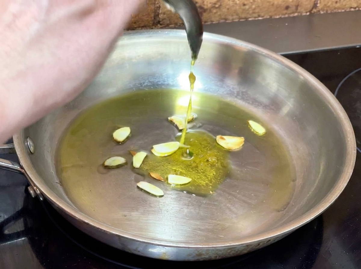 Knoblauchpaste wird mit einem Löffel in eine Pfanne mit aromatisiertem Öl und Knoblauchscheiben gegeben.