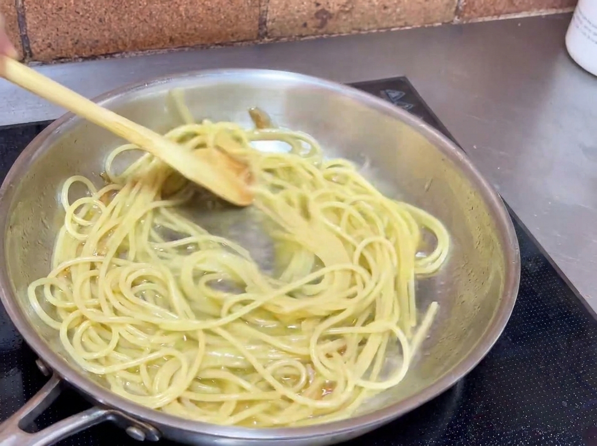 Spaghetti werden in einer Pfanne mit einem Kochlöffel geschwenkt, um die Nudeln mit der Knoblauch-Öl-Sauce zu überziehen.