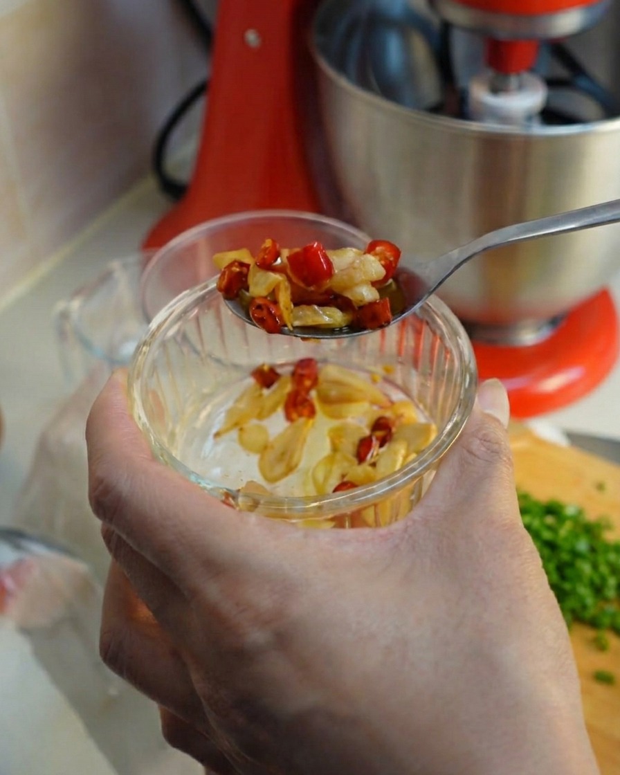 Ein Löffel schöpft frittierten Knoblauch und Chili aus einer kleinen Glasschüssel.