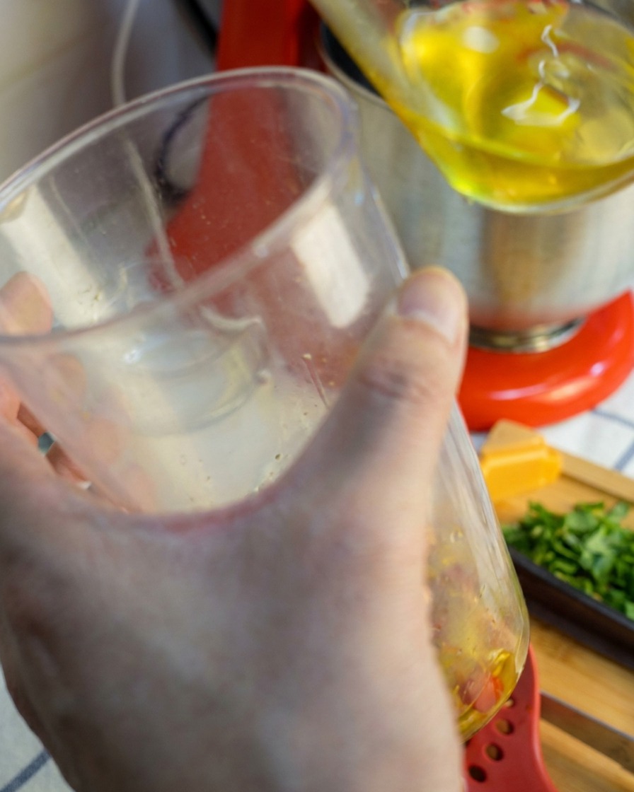 Ein Stabmixer wird aus einem Becher gehoben, an dem eine glatte, gold-rote Sauce haftet.