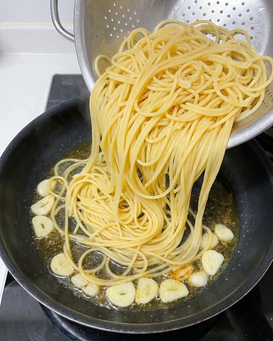 Gekochte Spaghetti werden aus einem Sieb in eine Pfanne mit aromatisiertem Öl gegeben.