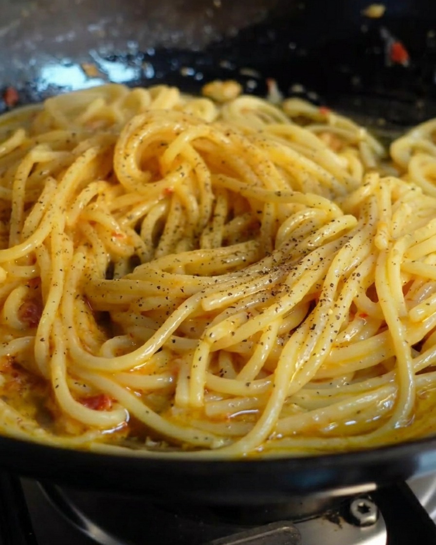 Frisch gemahlener schwarzer Pfeffer wird über die glänzenden Spaghetti gestreut.