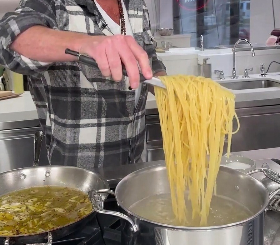 Noch nicht ganz gar gekochte Spaghetti werden mit einer Metallzange direkt aus dem kochenden Wasser gehoben.