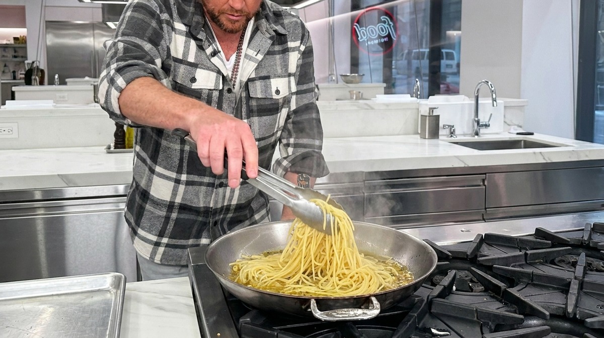 Spaghetti werden mit einer Zange in die heiße Pfanne zu Knoblauch, Öl und Nudelwasser gegeben.