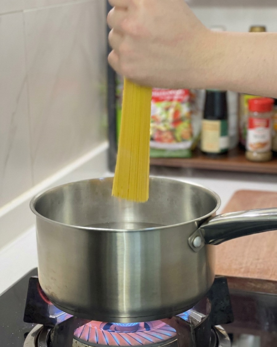 Eine Hand hält Spaghetti senkrecht über einen Topf mit kochendem Wasser.