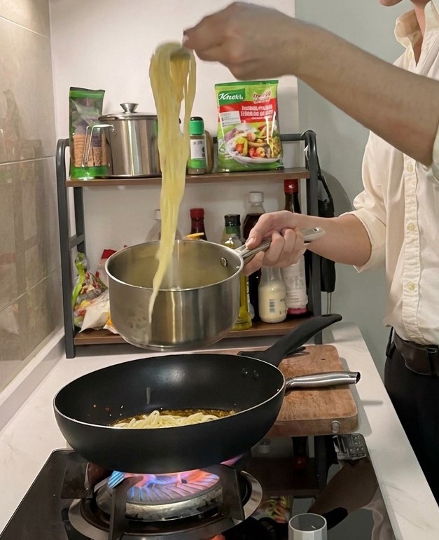 Spaghetti werden mit einer Zange aus dem Topf direkt in eine Pfanne mit Öl und Garnelen gehoben.