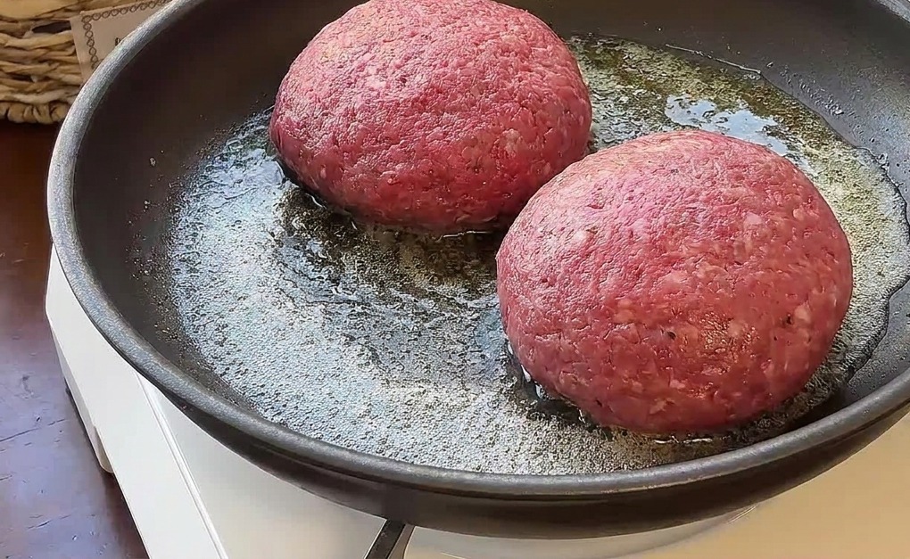 Zwei dicke gefüllte Burger-Patties werden in Butter in einer Pfanne gebraten.