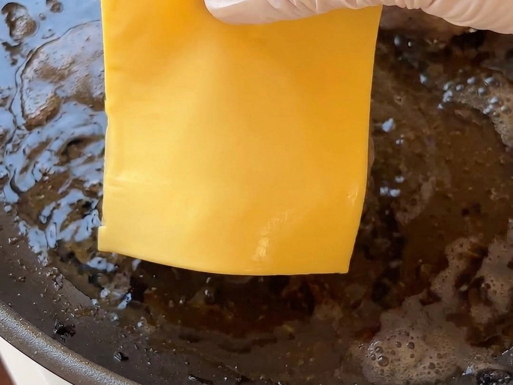 Eine Hand legt eine Scheibe Käse auf ein heißes Patty in der Pfanne.