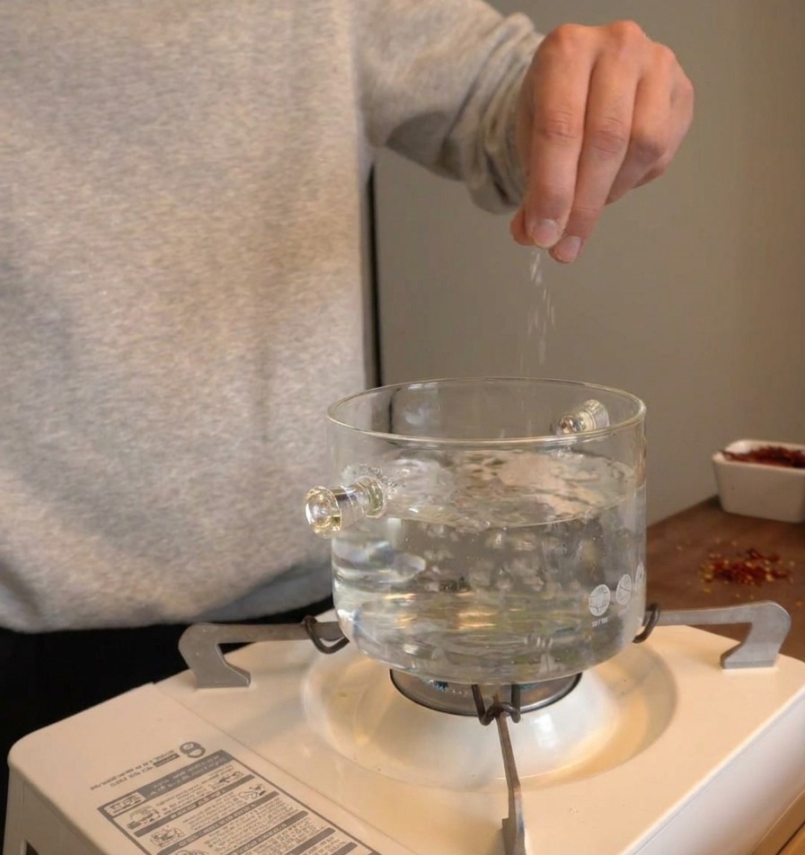 Eine Hand gibt eine großzügige Menge Salz in einen Topf mit sprudelnd kochendem Wasser.