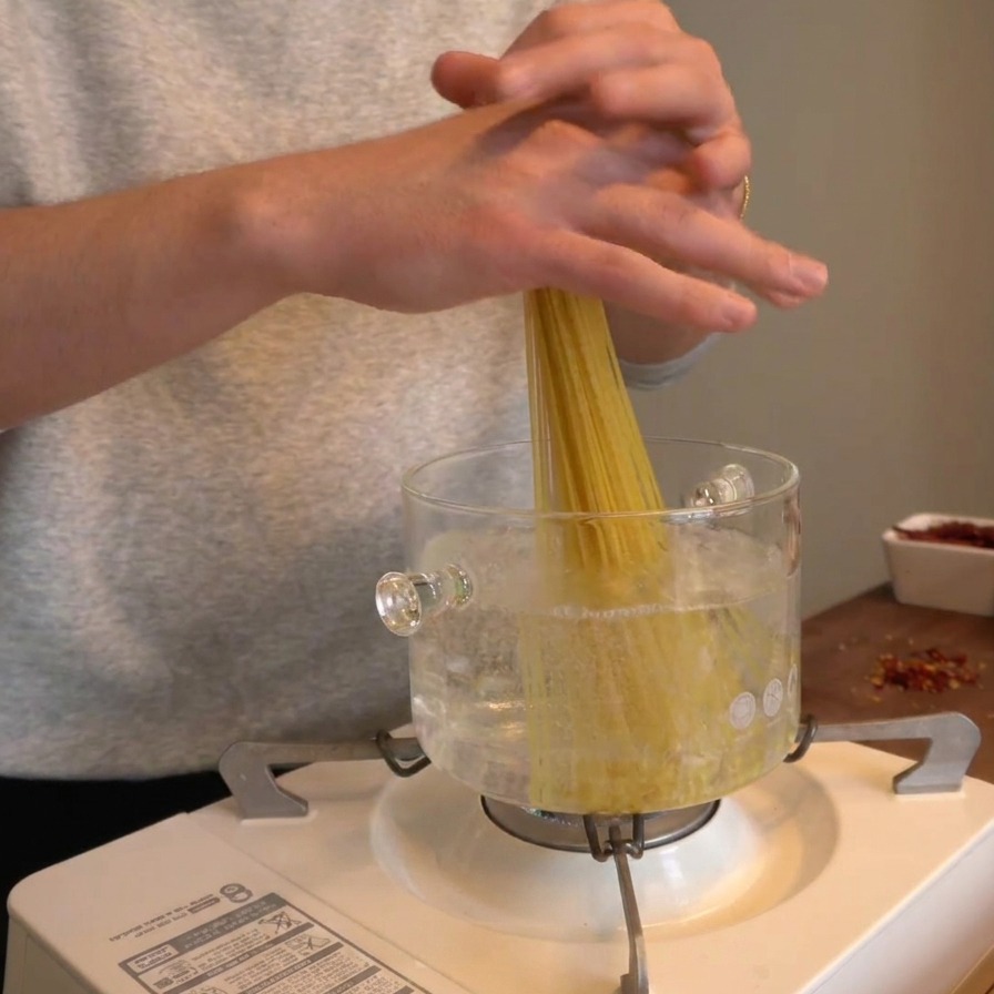 Hände geben ein Bündel trockene Spaghetti vertikal in einen Topf mit kochendem Wasser.