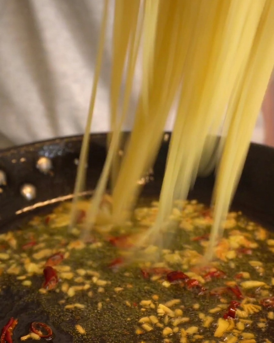 Lange Spaghetti-Stränge werden direkt aus dem Topf in die Pfanne mit der Knoblauch-Chili-Sauce gegeben.
