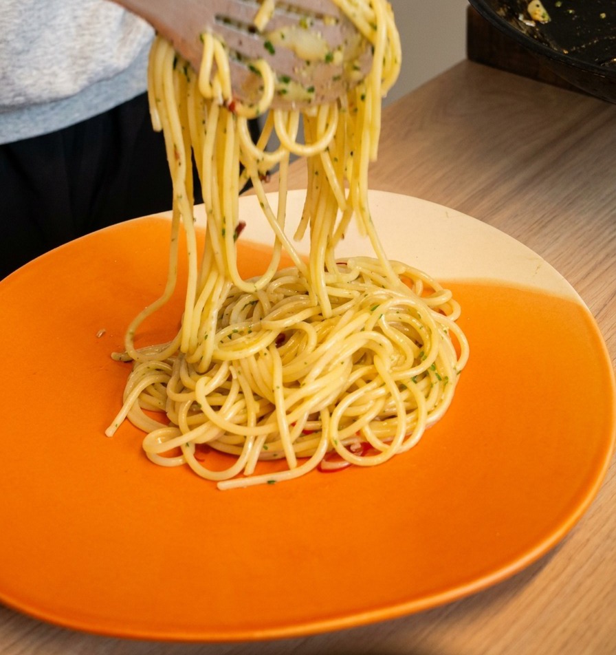 Küchenzangen heben Spaghetti aglio e olio an und platzieren sie eingedreht auf einem Teller.
