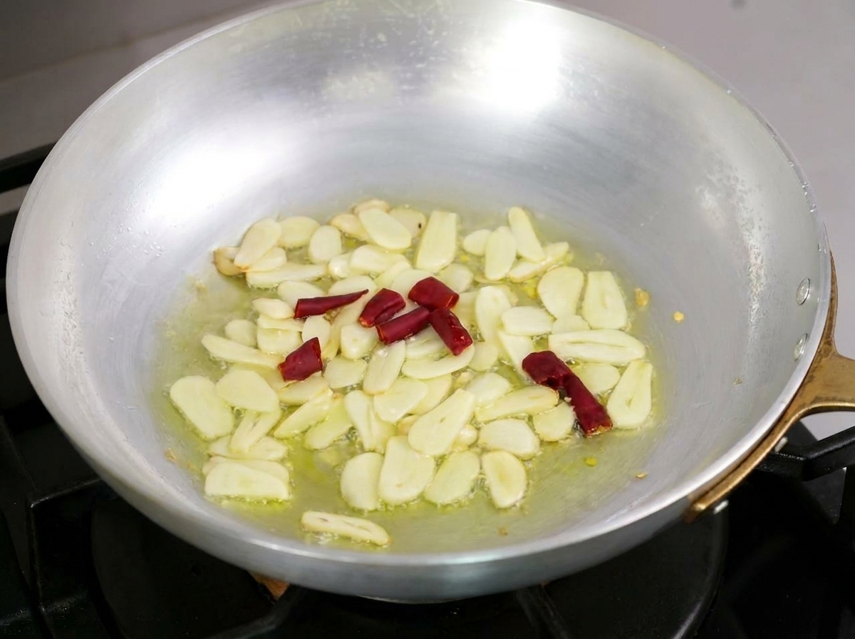 Geschnittener Knoblauch und Stücke von getrocknetem rotem Chili, die sanft in Olivenöl in einer Metallpfanne brutzeln.