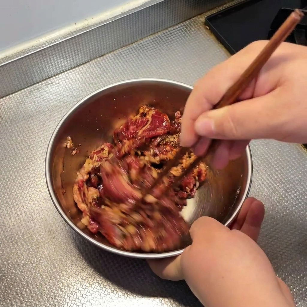 Rindfleisch wird mit Stäbchen in einer Metallschüssel kräftig umgerührt.