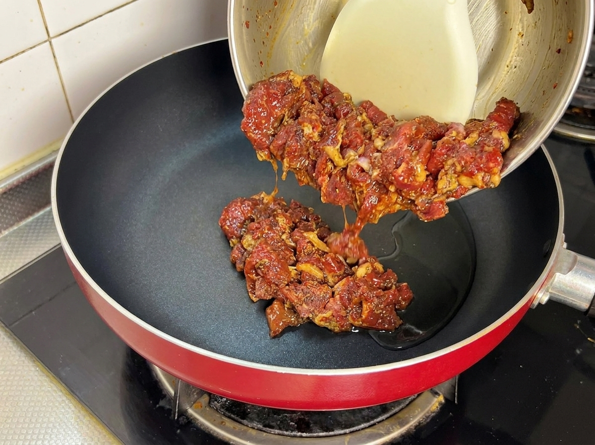 Mariniertes Fleisch wird in eine heiße Pfanne mit Speiseöl gegeben.