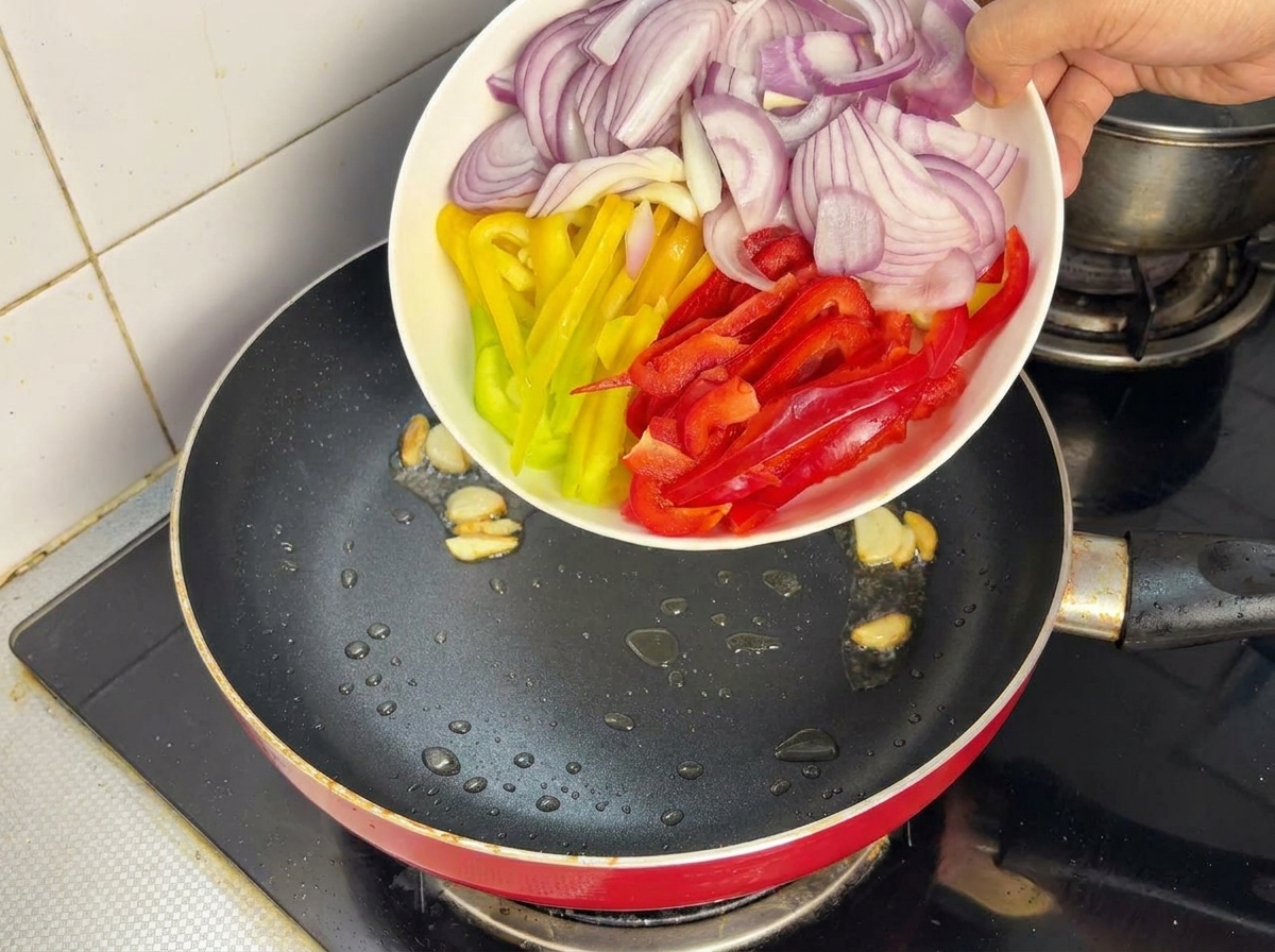 Zwiebeln und Paprika werden in der heißen Pfanne unter Rühren angebraten.