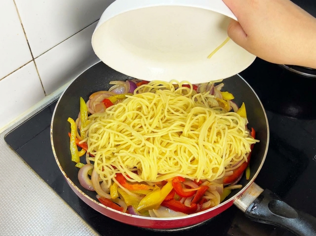 Das angebratene Fleisch wird wieder zu den Nudeln in die Pfanne gegeben.