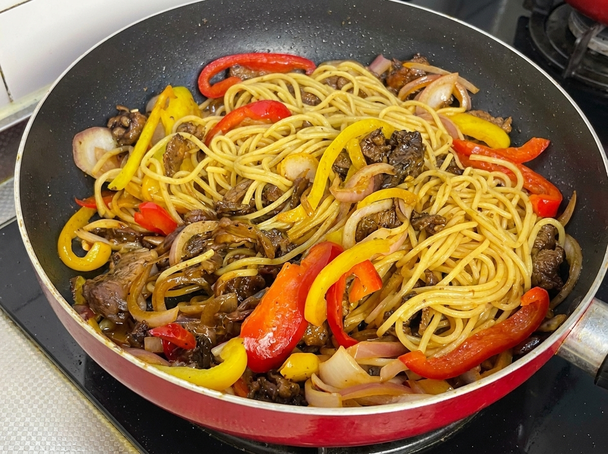 Die Spaghetti glänzen gleichmäßig mit der dunklen Sauce in der Pfanne.