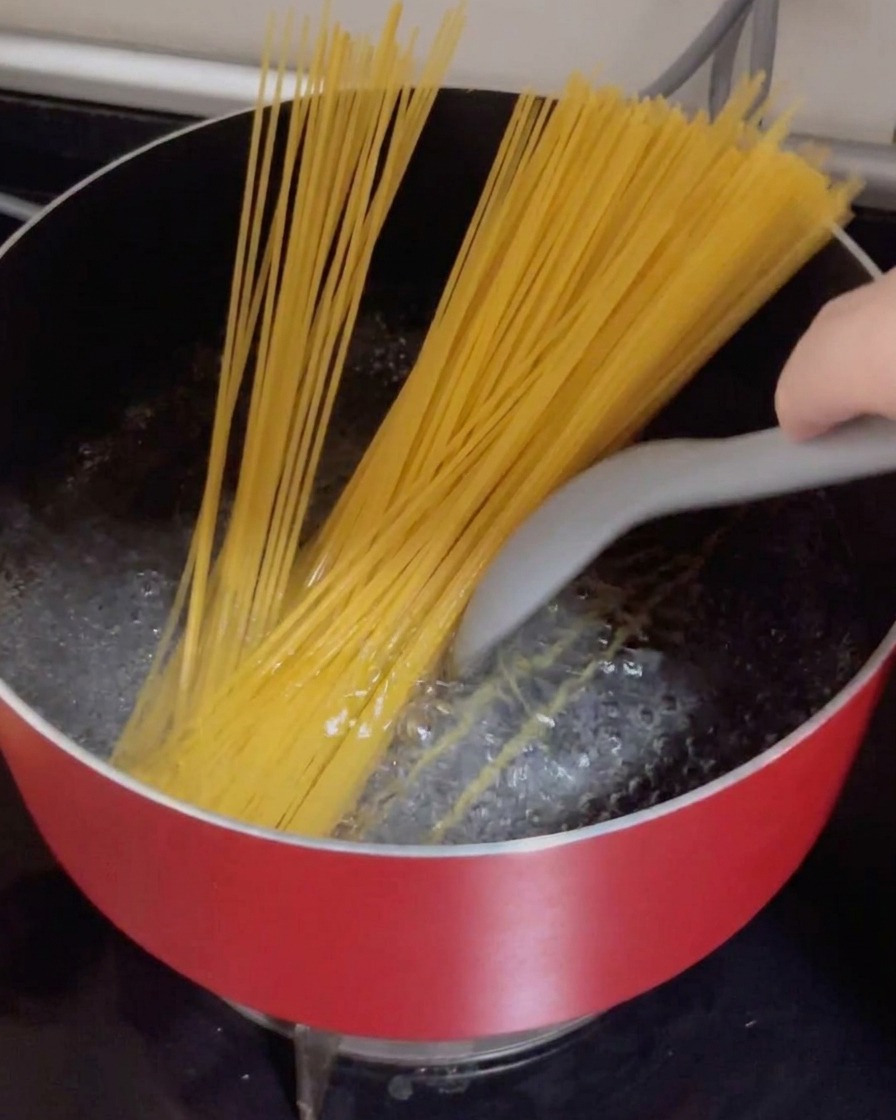 Trockene Spaghetti werden in einen roten Topf mit sprudelnd kochendem Wasser gedrückt.