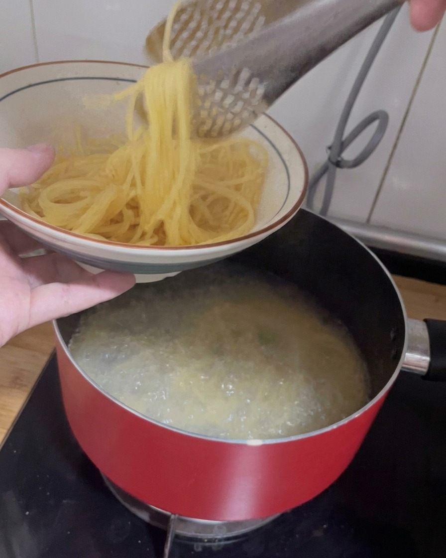 Eine Zange hebt gekochte Spaghetti aus dem heißen Wasser in eine gemusterte Keramikschale.