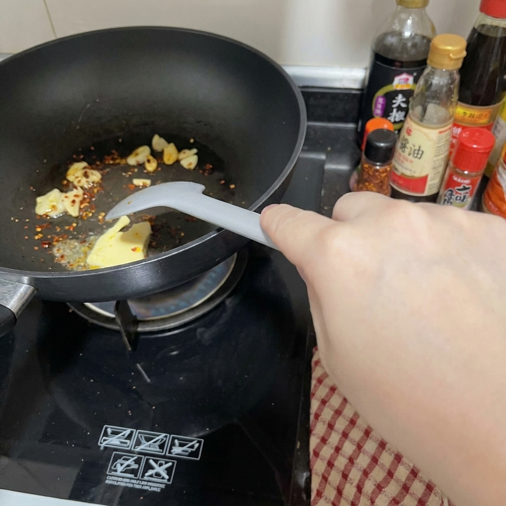 Ein Stück Butter schmilzt in einer schwarzen Pfanne neben Knoblauch und Chiliflocken und wird mit einem Spatel verrührt.