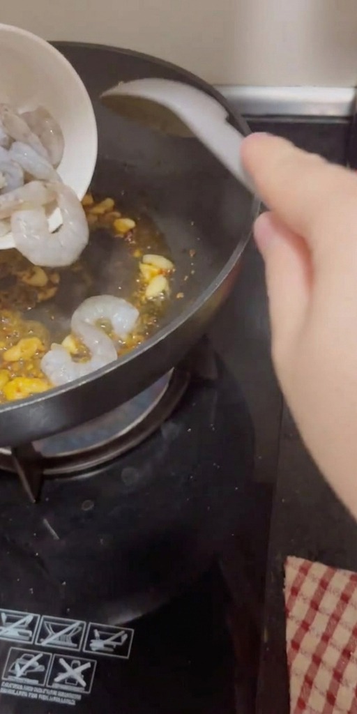 Rohe, geschälte Garnelen werden aus einer Schüssel in die heiße Pfanne zu Knoblauch und Chili gegeben.