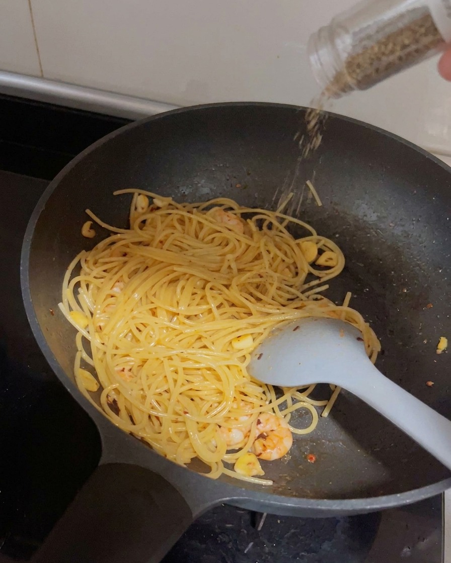 Eine Mühle mahlt frischen schwarzen Pfeffer über die Pfanne mit Spaghetti und Garnelen.