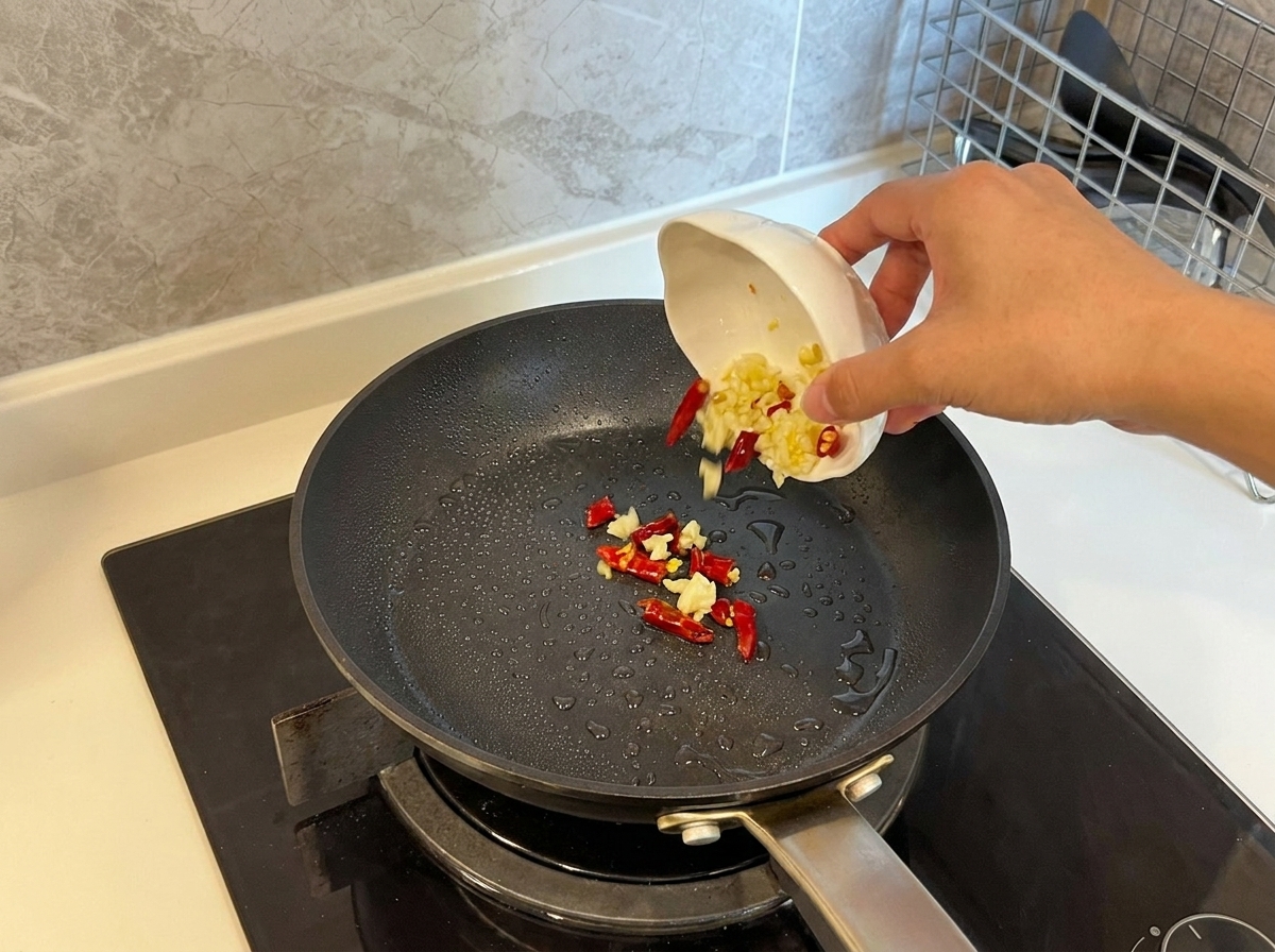 Knoblauchscheiben und getrocknete Chilischoten werden in eine heiße Pfanne mit Öl gegeben.