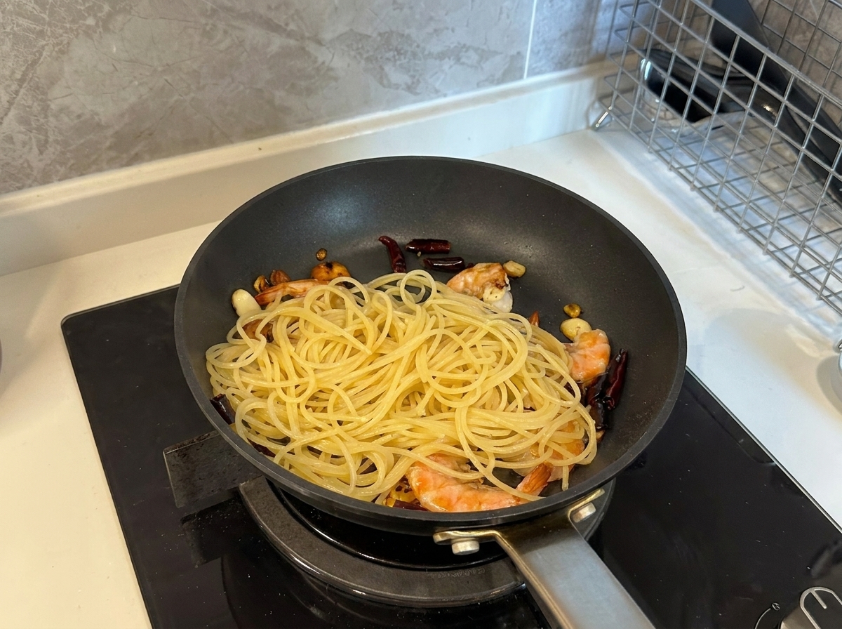 Gekochte Spaghetti werden zu den Garnelen und dem Knoblauch in die Pfanne gegeben.