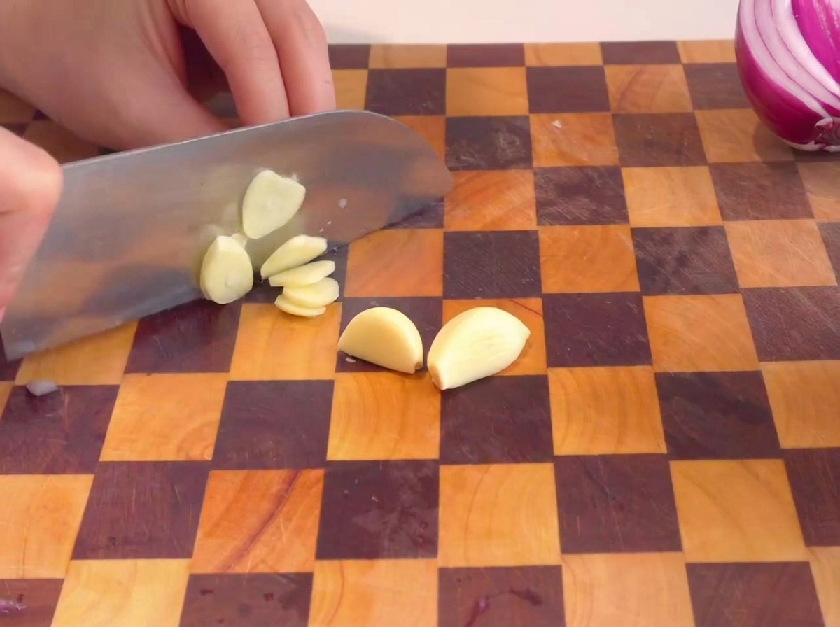Hände schneiden geschälten Knoblauch auf einem Schneidebrett in dünne Scheiben.
