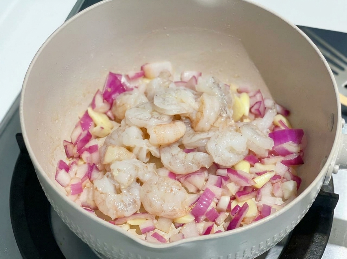 Rohe Garnelen werden zu den Zwiebeln in die Pfanne gegeben.