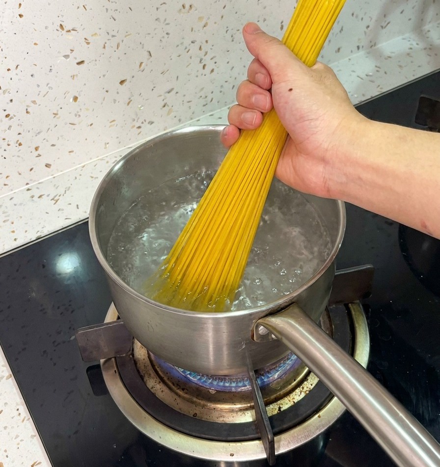 Eine Hand gibt trockene Spaghetti in einen Topf mit sprudelnd kochendem Wasser.