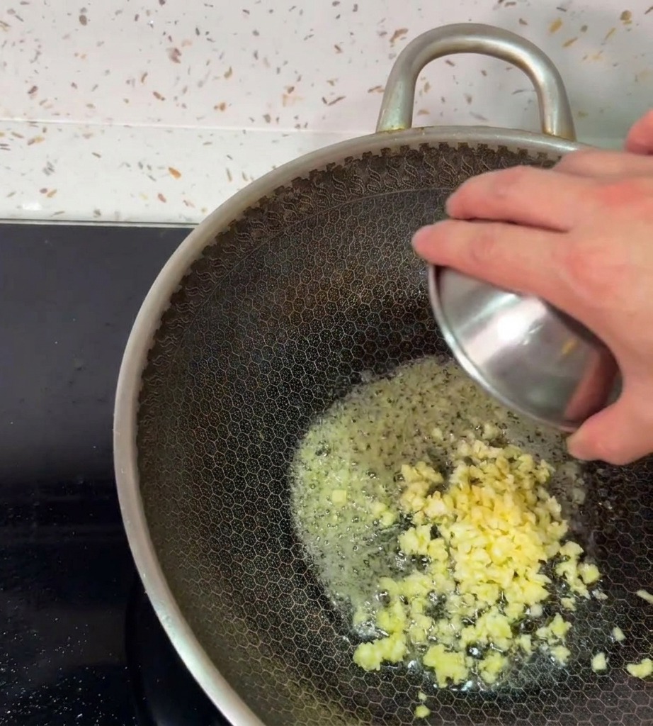 Gehackter Knoblauch wird aus einer kleinen Schüssel in die schäumende Butter im Wok gegeben.