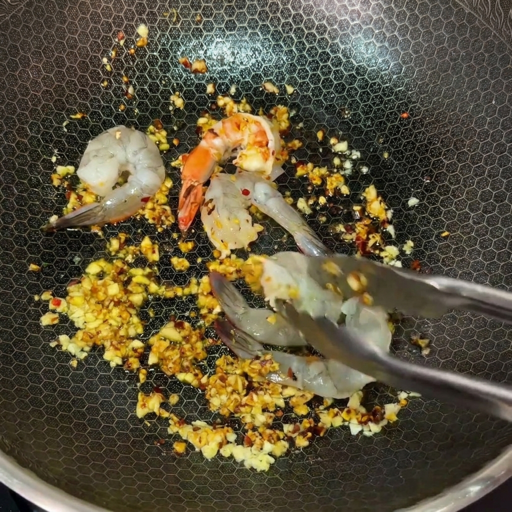 Rohe Garnelen werden mit einer Zange in den heißen Wok mit Knoblauchbutter gelegt.