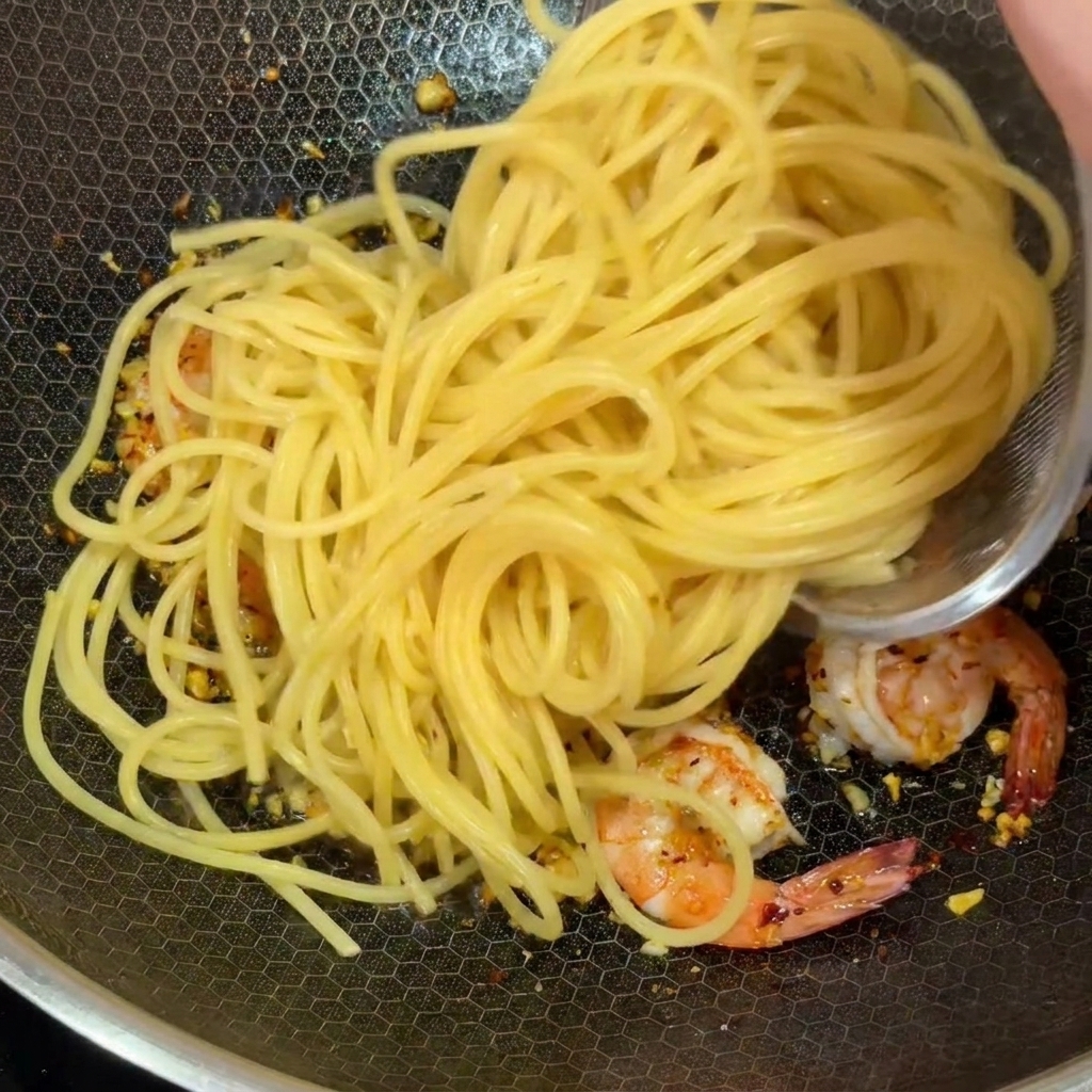 Gekochte Spaghetti werden zu den Garnelen und dem Knoblauch in den Wok gegeben.