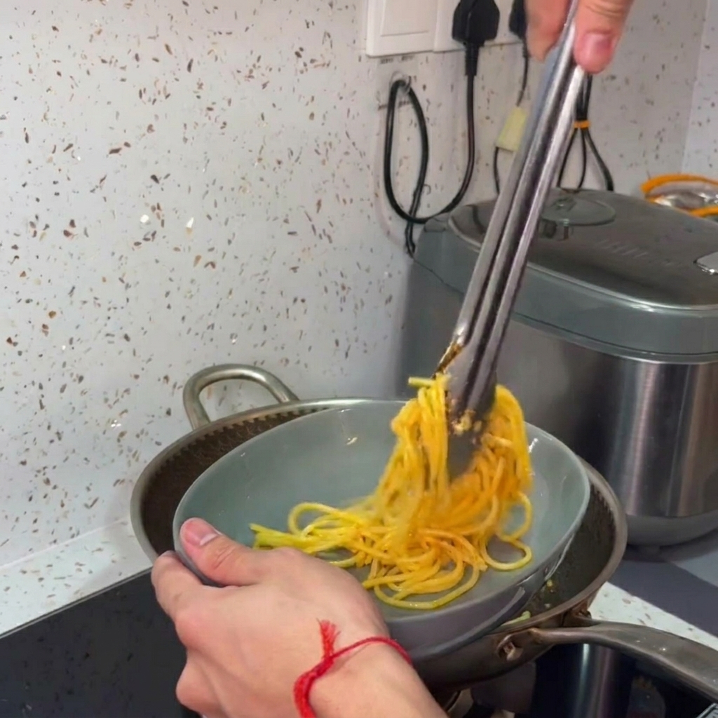Mit einer Zange werden die heißen Spaghetti nestartig auf einem Teller angerichtet.