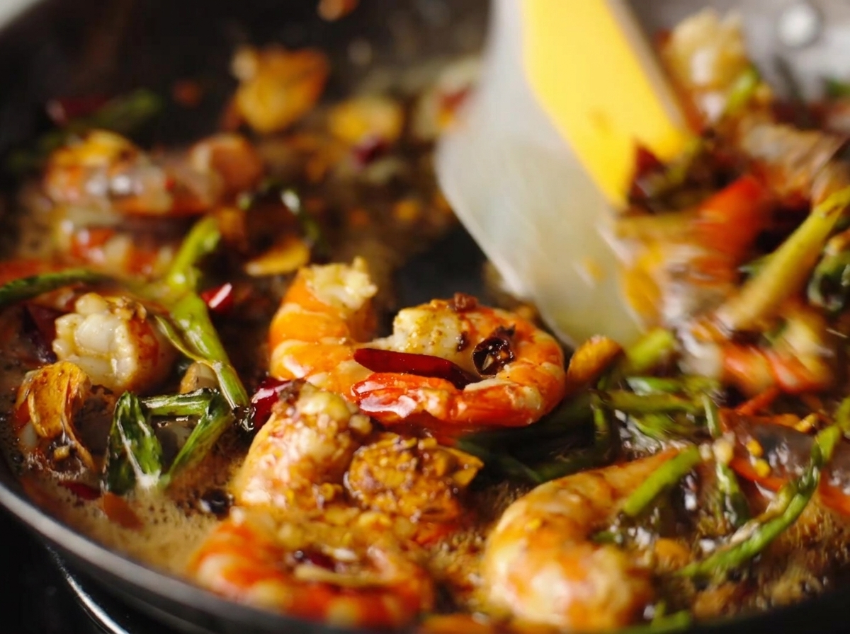 Geschälte Garnelen werden mit Knoblauch, Chili und Frühlingszwiebeln in einer Pfanne sautiert.