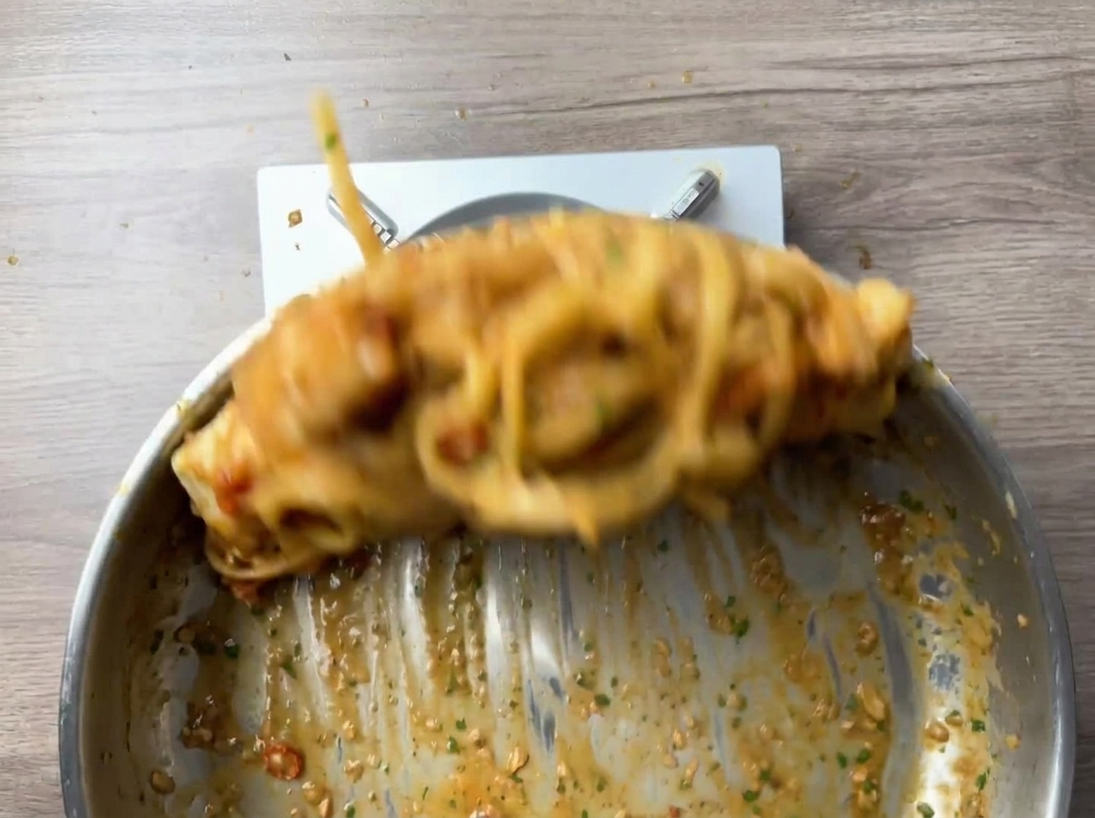 Pasta und Garnelen werden schwungvoll in der Pfanne geschwenkt.